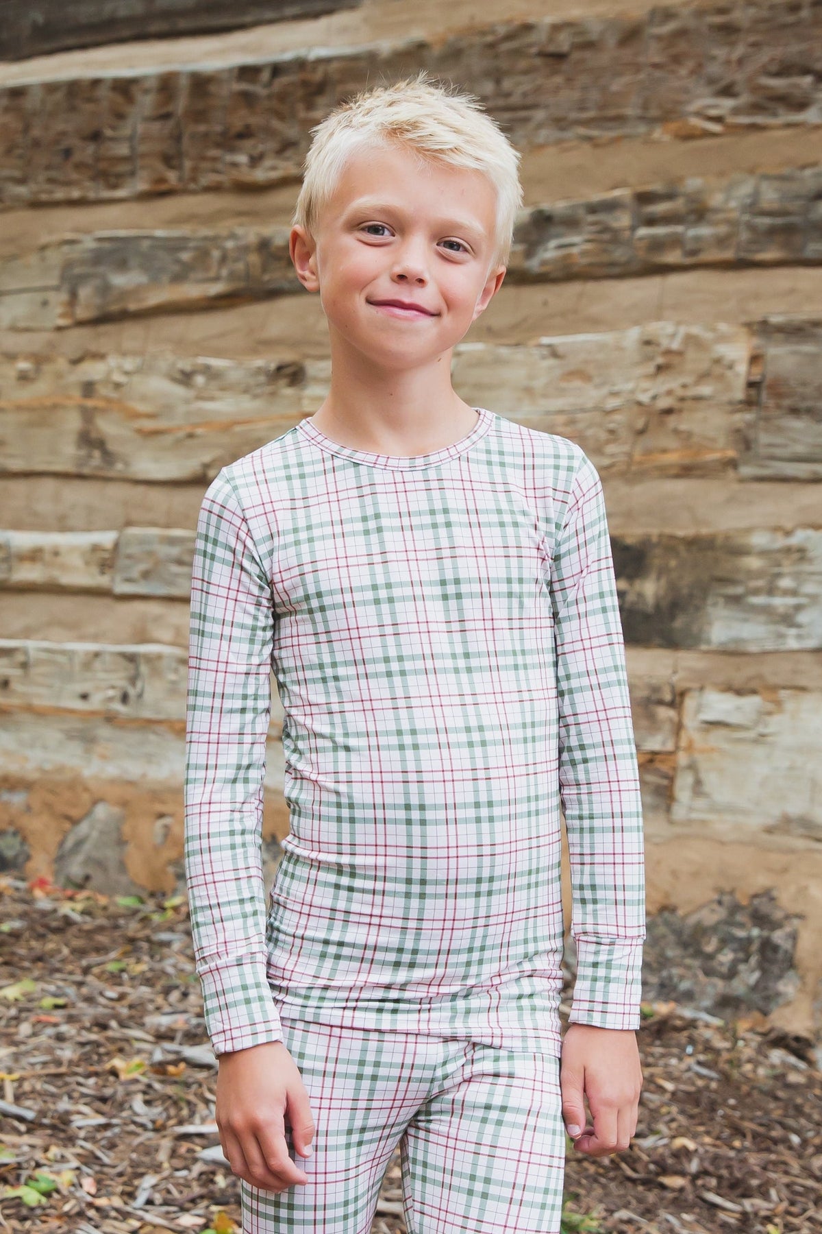 A young boy wearing homestead / two piece skinny long-sleeved plaid pajamas in a green and red pattern.