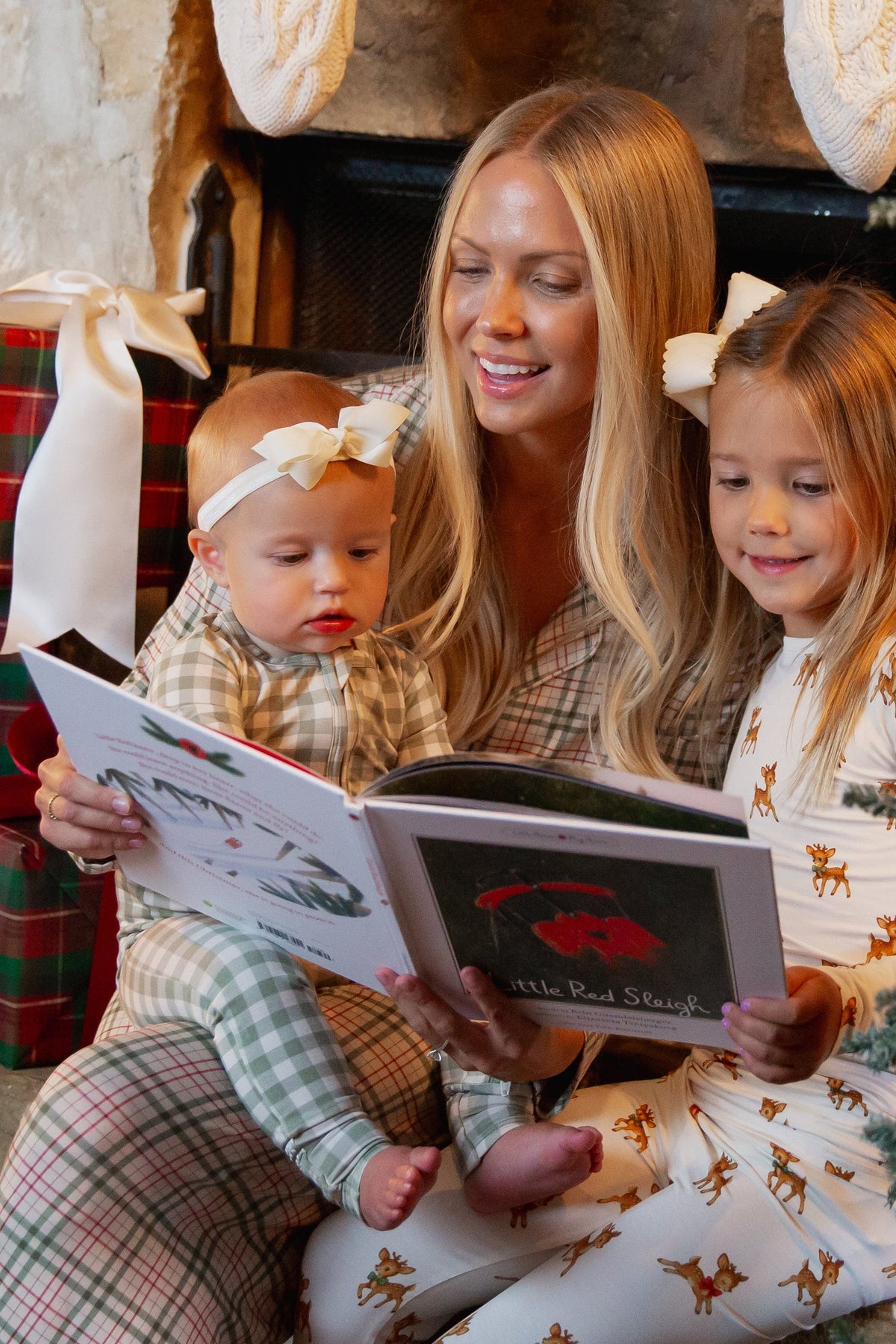 A woman and two young children wearing matching evergreen lane / one piece zipper bamboo pajamas sit together reading a storybook.