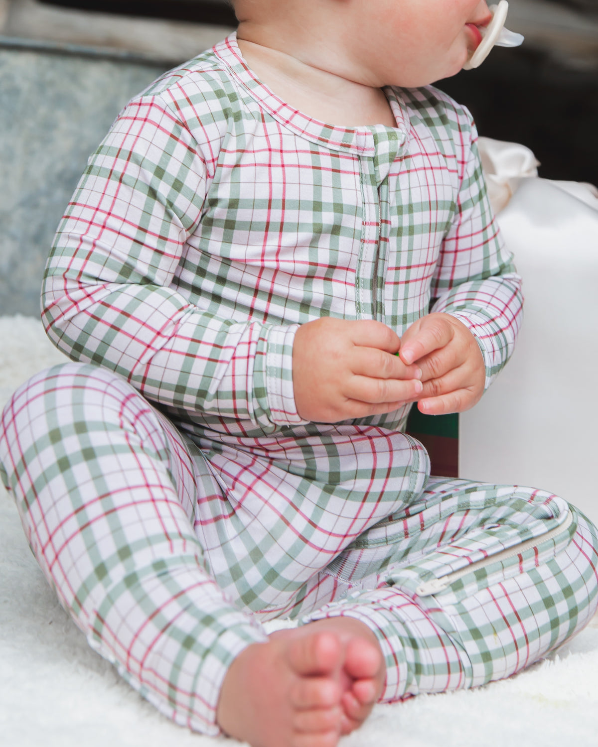 A baby wearing a green and red plaid homestead / one piece zipper with a front zipper and footed design.
