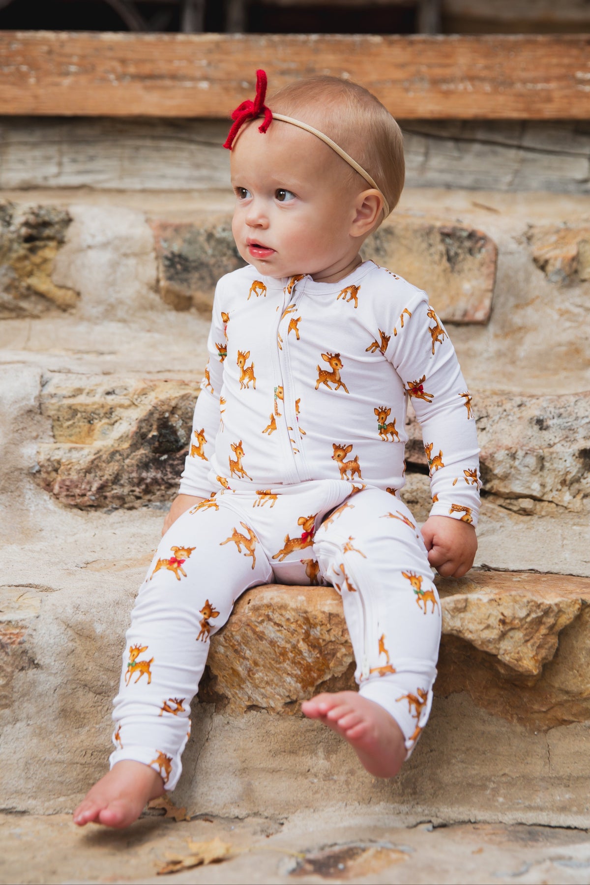 A baby wearing a white vintage reindeer / one piece zipper sits on stone steps.