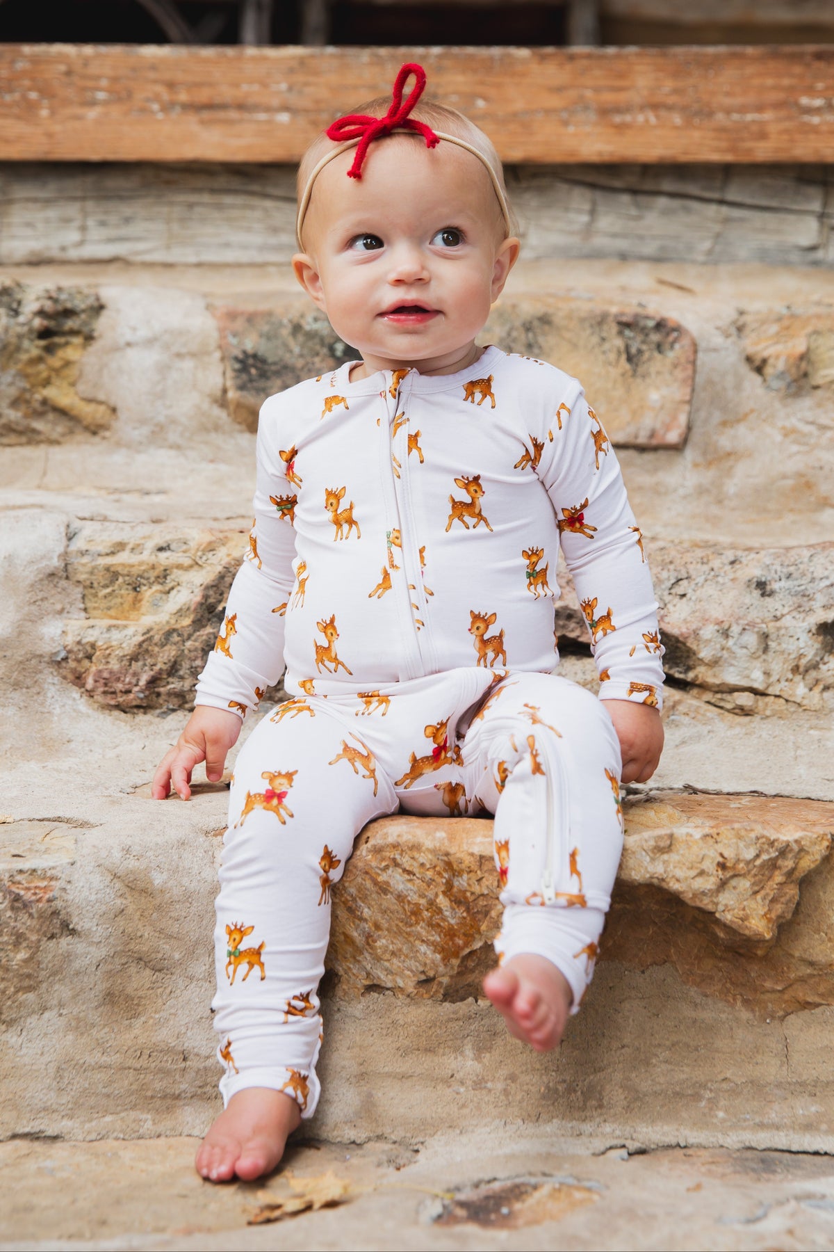 A baby sits on stone steps wearing a white long-sleeve vintage reindeer / one piece zipper with a reindeer print.