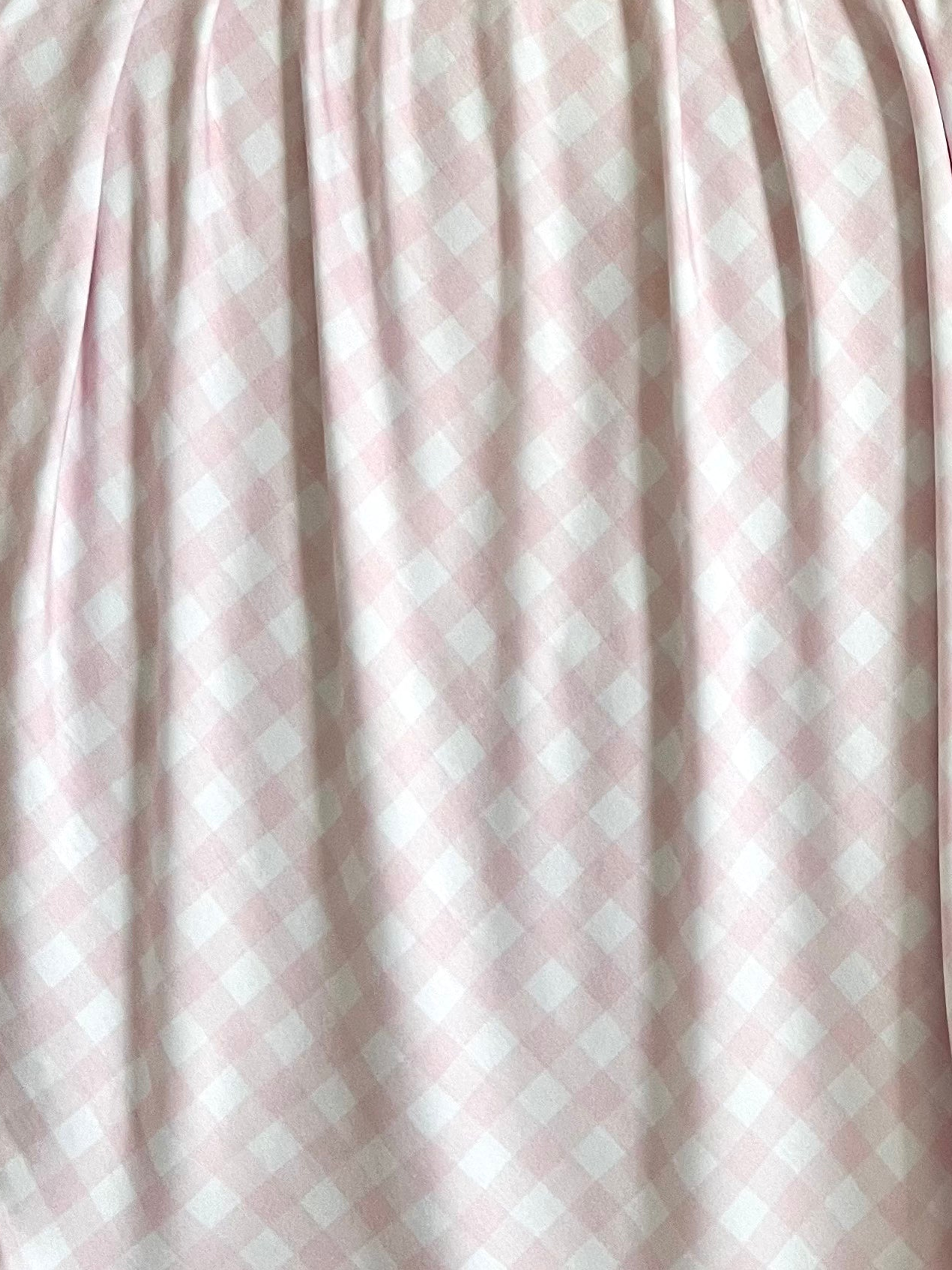 The xo / swaddle features light pink and white bamboo gingham fabric with a diamond checkered pattern, softly gathered to create gentle shadows and highlights across its surface.